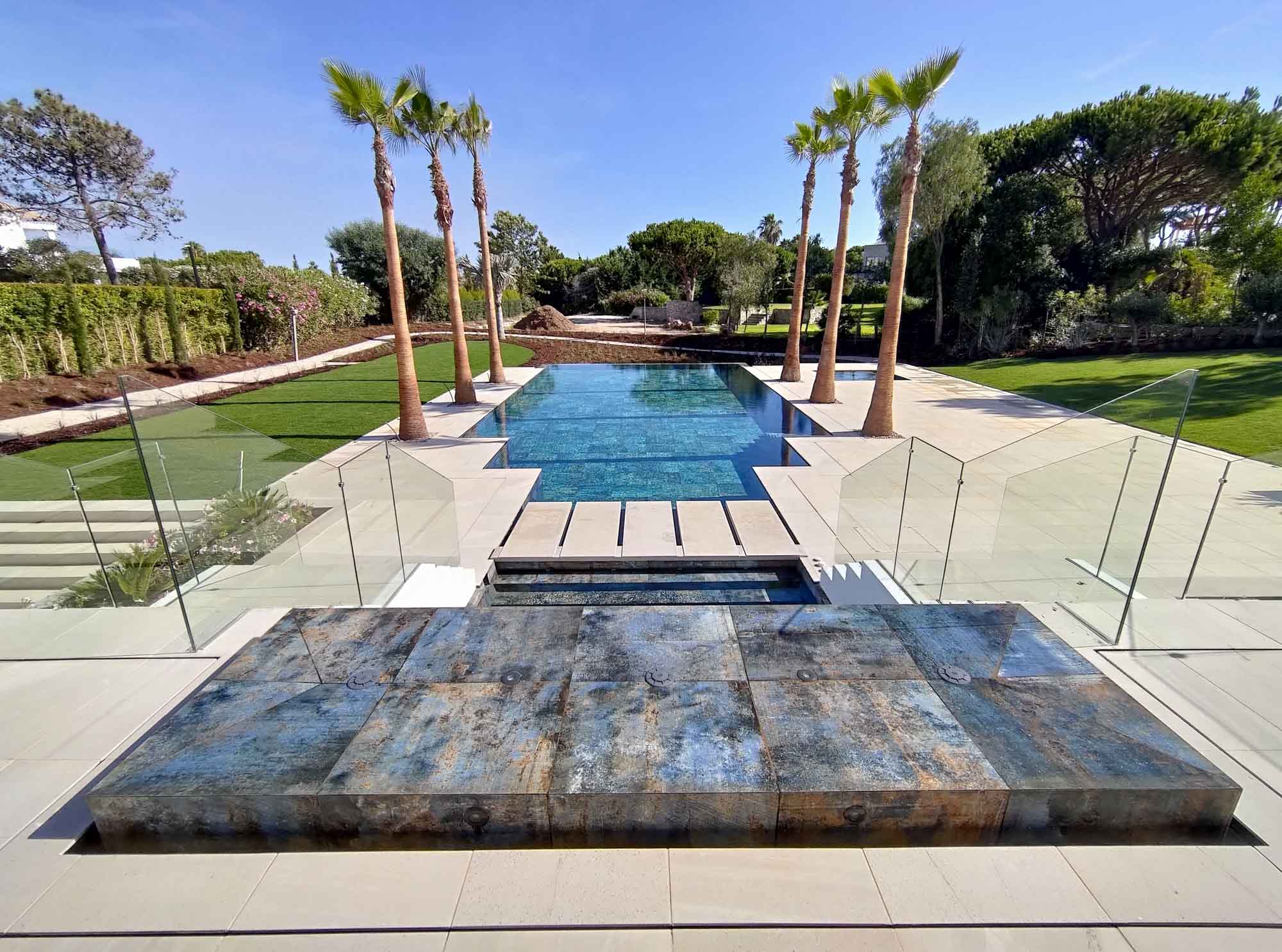 Panorámica de piscina en villa privada de lujo, rodeada de palmeras, con zona de spa y amplia playa par tomar el sol